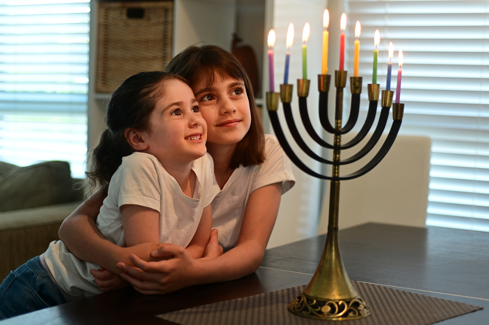 Two happy Jewish sisters looking at a beautiful menorah candelabra glowing on the eight day of Hanukkah Jewish holiday